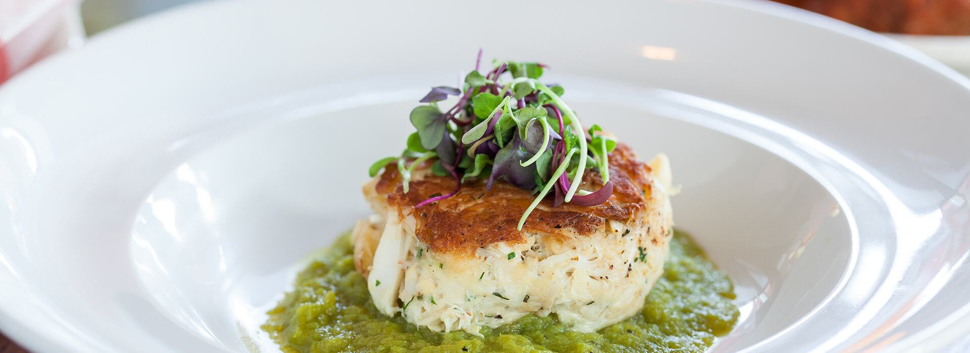 Crab cake on sauce topped with greens