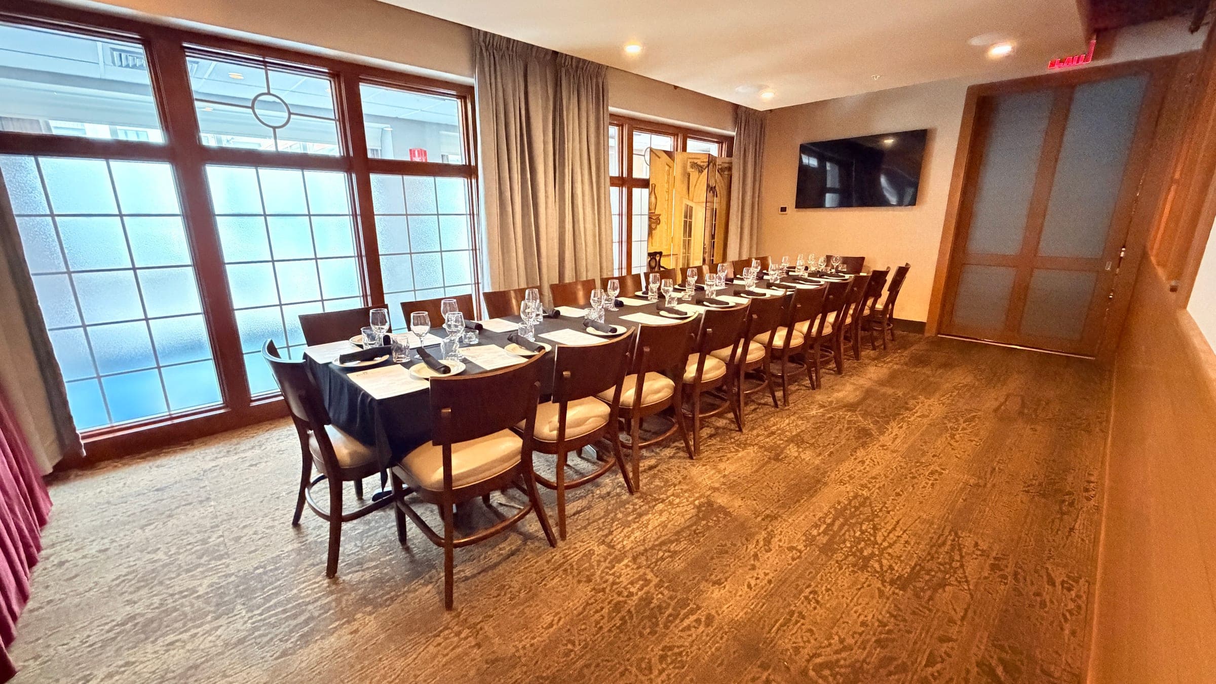 Private dining room with frosted windows, AV screen, and a long table set for twenty